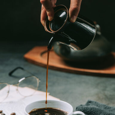 A close-up of a hand pouring coffee water into a coffee cup, international coffee day concept