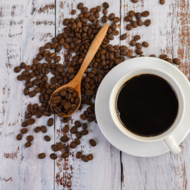 Coffee cup and coffee beans in wooden spoon on white table. Top view.